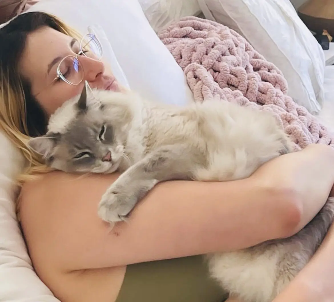 Kimberly napping with a fluffy gray cat snuggled in her arms